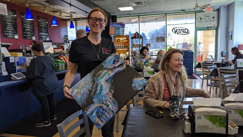 Local photographer and painter Deanna Gibson holds a painting at The Curator's Cafe in Joliet on Saturday, April 13, 2024.  Gibson will create art during the Joliet Symphony Orchestra’s “Pictures” performance on Saturday and Sunday.