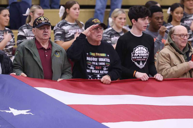 Veterans and students from Lincoln-Way West and Lockport hold the notable flag that flies along I-80 during the Nation Anthem at the Lockport Township High School 10th Annual Veterans Night Celebration on Friday, Dec. 6, 2024.