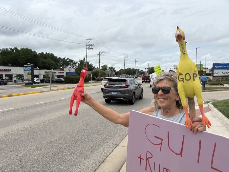 Kathryn Koeune squeezes a chicken that reads "Taco" during a protest in McHenry July 26, 2025.
