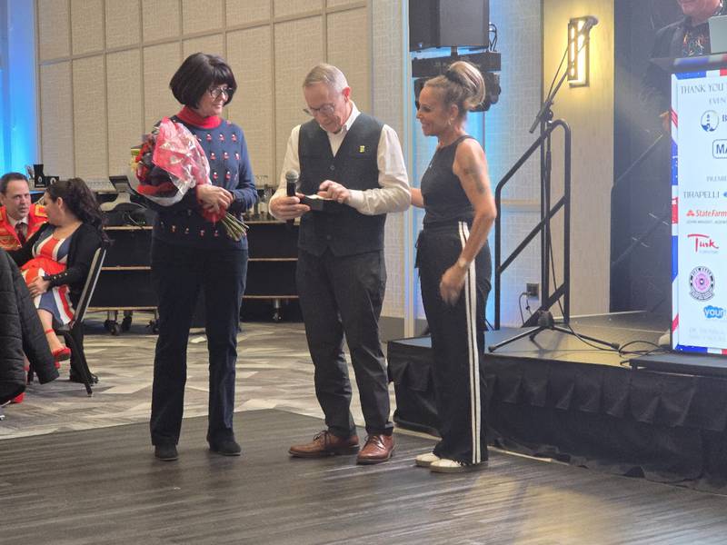 Laura Charland, Shorewood HUGS co-founder (right) presents Dr. Thomas and Nancy Moore with the Lynne Lichtenauer Community Service Award for their longtime support at the Shorewood HUGS' "Lovely London: A Big Ben Bash" 2026 chocolate ball fundraiser on Saturday, Feb. 7, 2026, at Hollywood Casino Joliet.