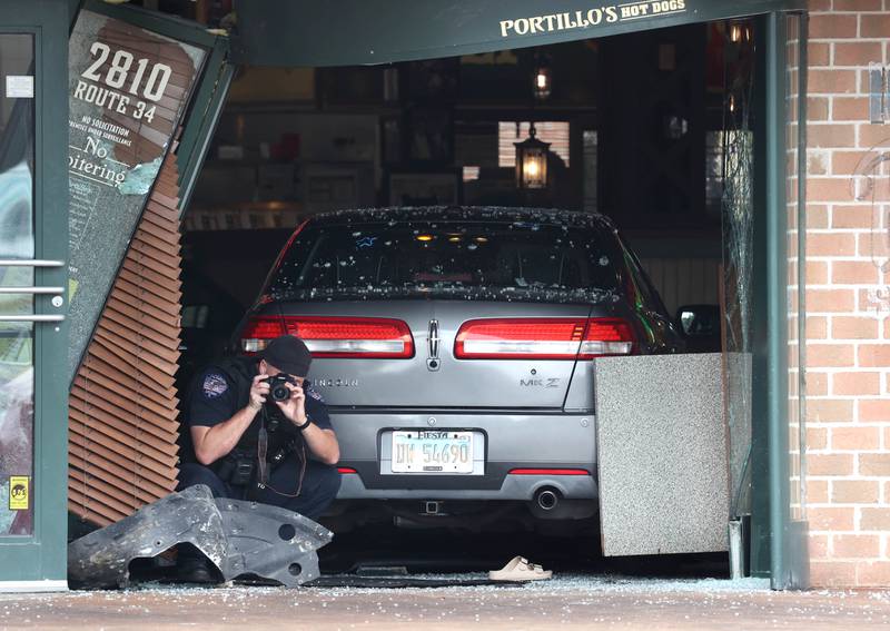 An Oswego Police officer photographs the scene Wednesday, July 30, 2025, where a car crashed through the front entrance of the Portillo’s at 2810 U.S. Route 34 in Oswego injuring 12.