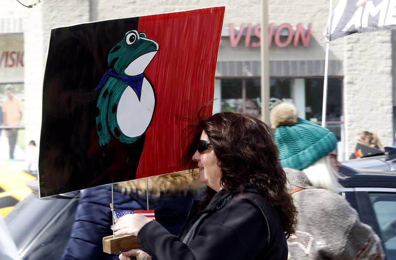 A women was with a sign of the protest frog as she protests with others as they line State Route 31 near the intersection of McCullom Lake Road in McHenry to protest their discontent with President Donald Trump and his administration's policies on Saturday, March 28, 2026, during the McHenry County No Kings Protest. According to an organizer, over 4,000, people took part in the protest.