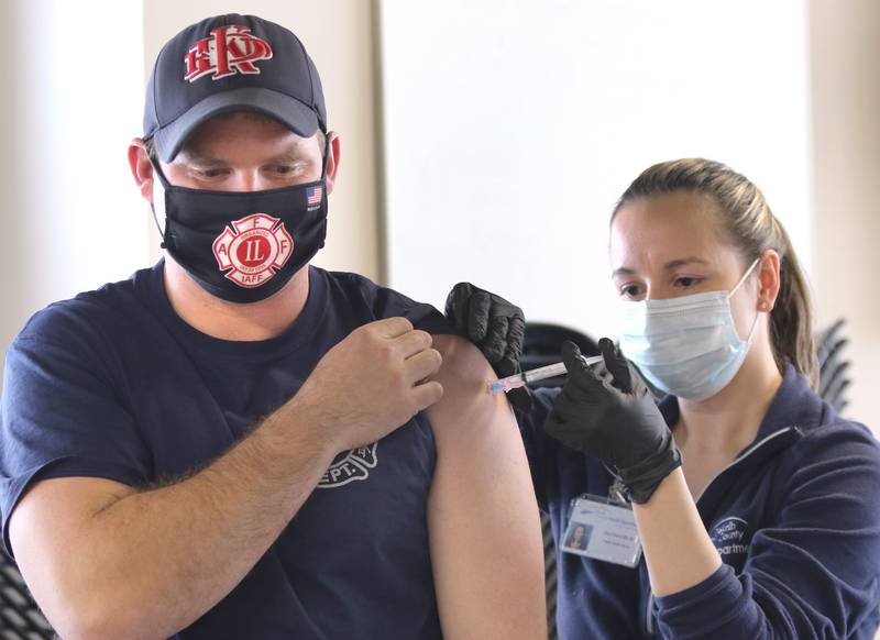 Adam Miller, a City of DeKalb firefighter/paramedic, receives an injection of the Moderna COVID-19 vaccine from DeKalb County Health Department public health nurse Alex Diehl Thursday in DeKalb.