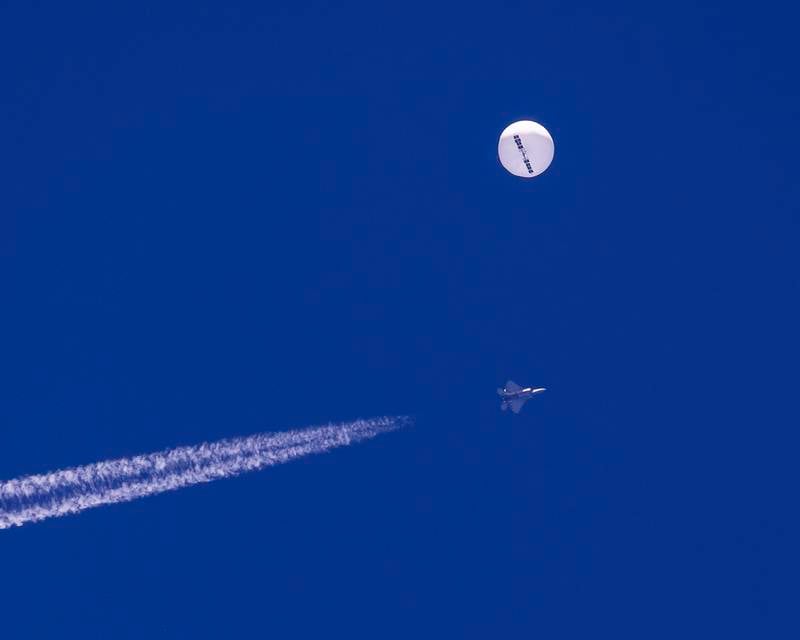In this photo provided by Chad Fish, a large balloon drifts above the Atlantic Ocean, just off the coast of South Carolina, with a fighter jet and its contrail seen below it, Saturday, Feb. 4, 2023. The balloon was struck by a missile from an F-22 fighter just off Myrtle Beach, fascinating sky-watchers across a populous area known as the Grand Strand for its miles of beaches that draw retirees and vacationers.  (Chad Fish via AP)