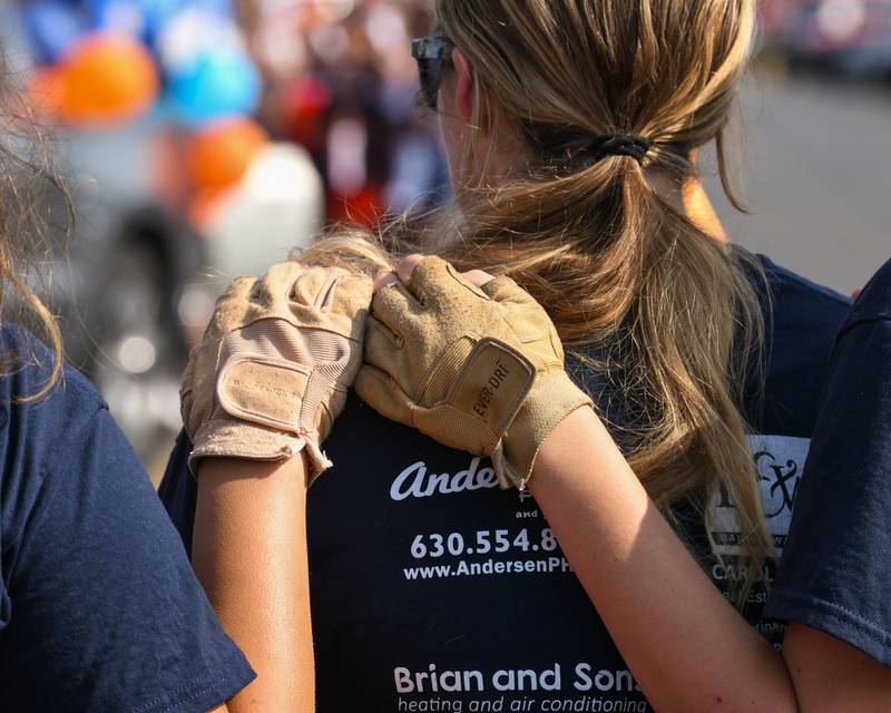 Oswego High School color guard members get comforted as the band plays Amazing Grace on Sunday Sept. 15, 2024, before the start of the homecoming parade to honor a classmate who passed away in a car crash.