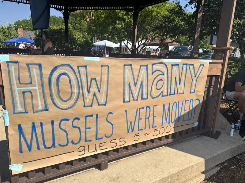 A sign asks marketgoers to guess the number of mussels removed from the site of the East Riverwalk on the Kankakee River at the Kankakee Farmers Market on Saturday, July 5, 2025. The inquiry was led by the Currents of Kankakee following the removal and relocation of endangered mussels at the construction site.