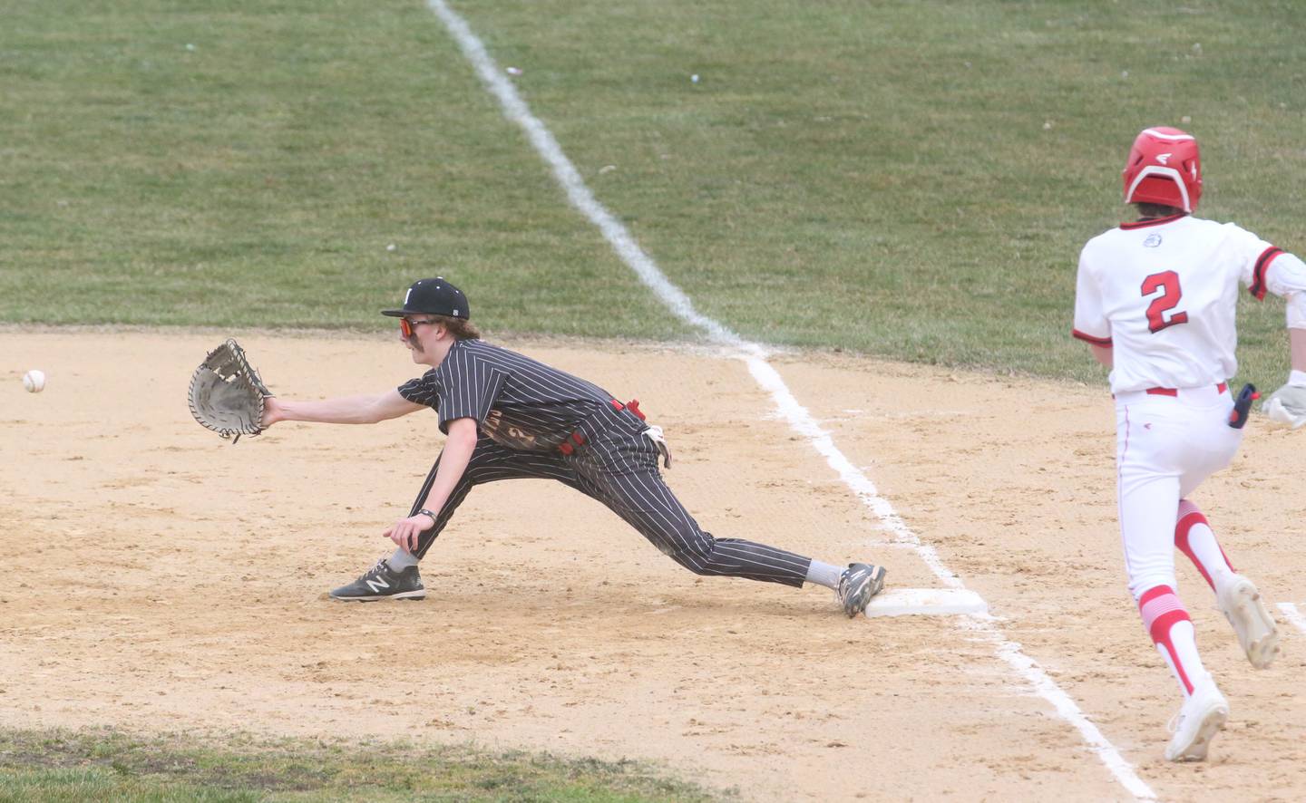 Hall's Izzaq Zrust stretches to catch the ball at first base to force out Streator's Zander McCloskey while Cole Winterrowd scores the go-ahead run Wednesday, March 13, 2024, at Kirby Park in Spring Valley.