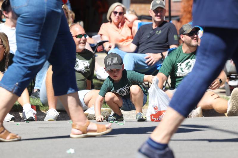 Dempsey Reynolds, 4, of Herscher, collects candy during the 104th annual Herscher Labor Day Celebration Grand Parade on Monday, Sept. 1, 2025. His dad, CJ Reynolds, right, and grandpa, Adam Wagner, left, all wear matching shirts in support of the Pop's Wagner Farms team in the weekend's softball tournament.