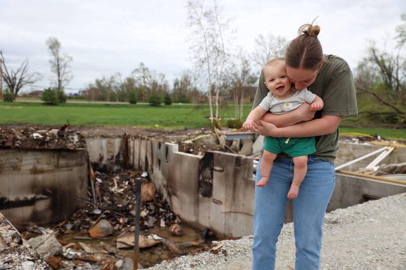 Erin Boerschig, a resident of Oakwoods subdivision in Aroma Township, holds her 8-month-old son Sawyer, on April 15, 2026, outside the basement where she sheltered with the Gerth family and pets during the March 10 tornado that hit Aroma Township. The Gerth's home on Waldron Road was leveled in the storm.