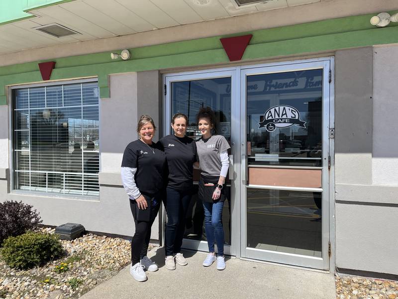 Owner Nete Bekteshi (middle) and two servers, standing in front of glass doors in front of black and white "Ana's Cafe" sign.