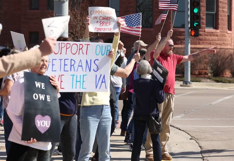 Protesters acknowledge honking cars as they gather to voice their displeasure with President Donald Trump Friday, March 14, 2025, in front of the DeKalb County Courthouse in Sycamore. The group was protesting recent cuts by the Trump administration to the Department of Veterans Affairs.
