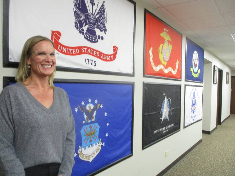 Jen Solum, Air Force veteran and superintendent for the Veterans Assistance Commission of Will County, stands along a wall of military banners at the VAC offices in Joliet. Oct. 20, 2025
