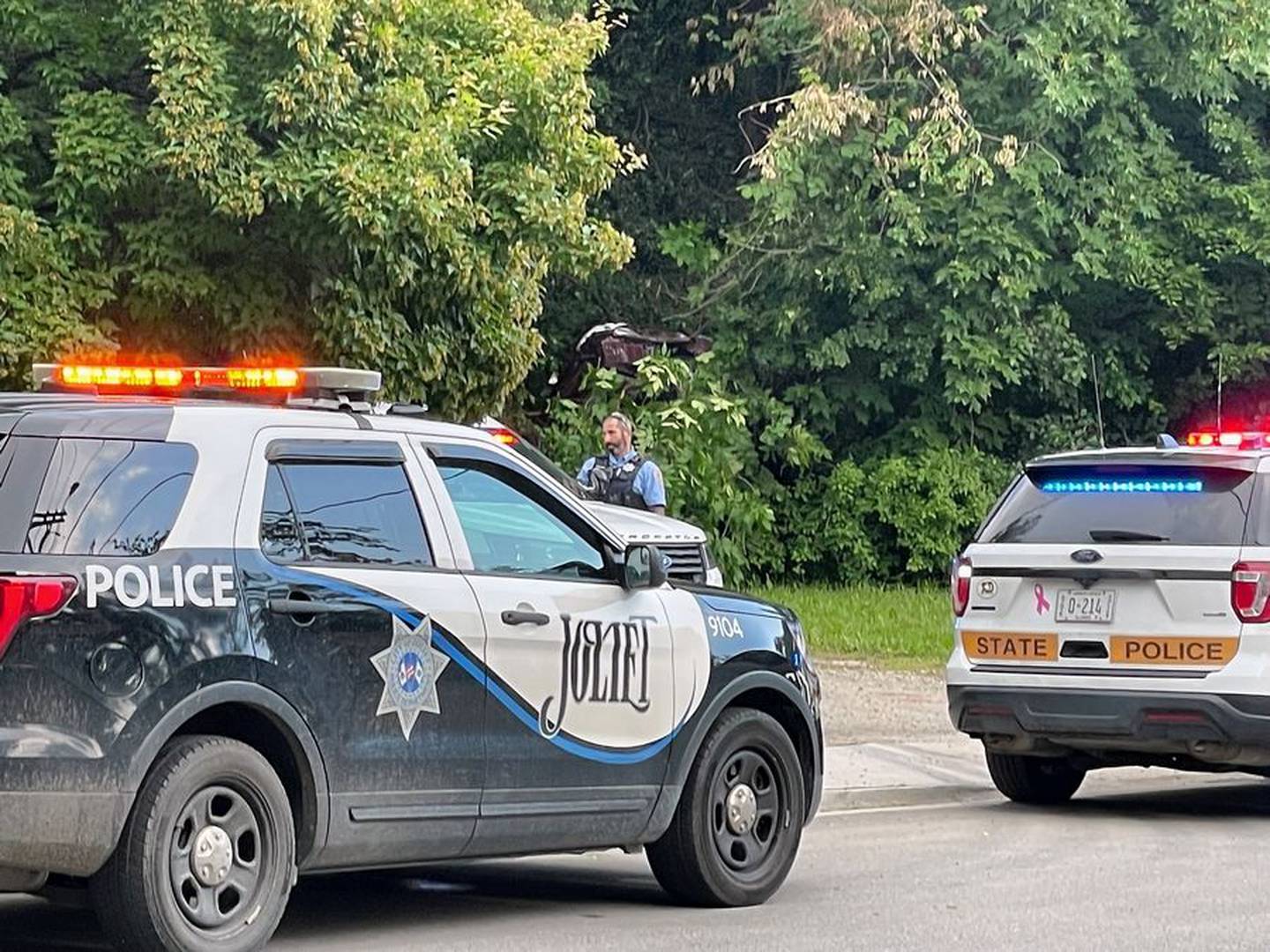 Police work the scene of a crash in which a vehicle connected to a triple homicide in Round Lake Beach rolled off an Interstate 80 highway bridge into trees and bushes in a Joliet neighborhood.