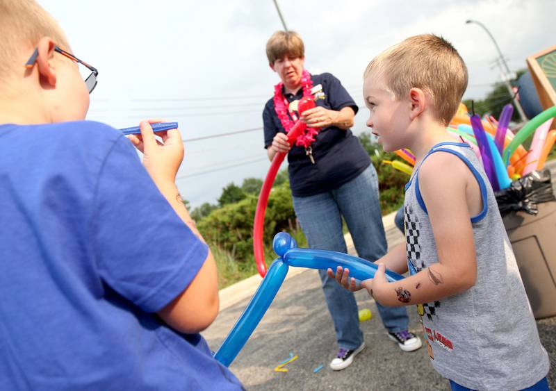 Nolan Burch (right), 3, plays with his balloon as library executive director Sarah Tobias (center) makes a balloon for Austin Burch (left), 6, at Sycamore Library's first beach party on Friday, August 1, 2014.