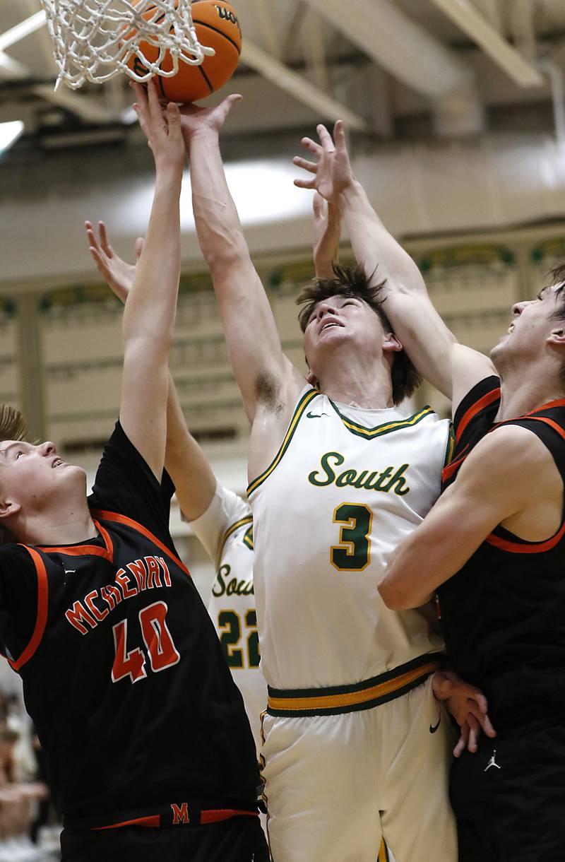 Crystal Lake South's Nick Stowasser (center) tires to tip a rebound into the basket between McHenry's Nate Ottaway (left) and  Carter Sites (right) during a Fox Valley Conference basketball game on Friday, Jan. 31, 2025, at Crystal Lake South High School.