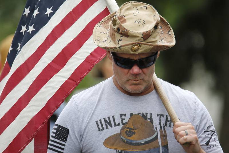 Police officer and former Marine Tim Mitsven carries a large American Flag as he listens to the Memorial Day ceremony on Monday, May 31, 2021 in Crystal Lake. The parade began at Crystal Lake Central High School and continued through downtown, ending at Union Cemetery with a ceremony.
