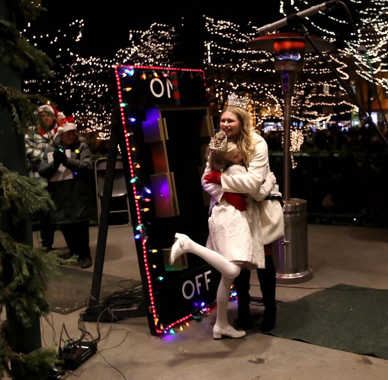 Little Miss Woodstock Myla McAdow hugs Miss Woodstock Kiera Merrell after they flipped the switch to turn on the lights during the Lighting of the Square on Friday, Nov. 28, 2025, in Woodstock.