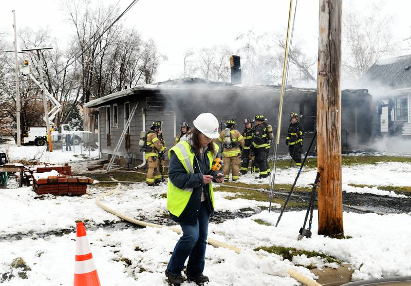 A NiGas worker walks by the charred remains of a home in Byron at 115 W. Third Street on Saturday morning. One woman was declared dead after being found outside the home after a power line fell on the house causing to become "electrified,"  a fire official said.