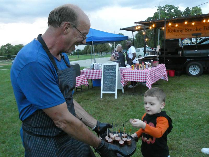Ken Midge, owner of Rolling Smoke Barbecue Food Truck, shown here offering samples of his Italian sausage at Blues and Brews Fest in McHenry on Aug. 20, 2022, says he warns clients in advance that certain items like wings will cost extra these days.