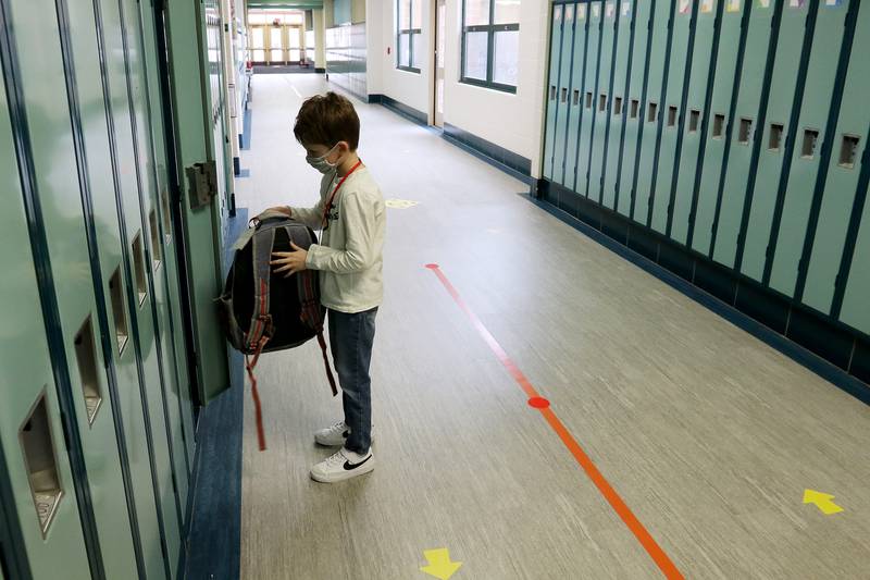Colin Marks, a second-grade student at Woods Creek Elementary School, puts his backpack into his locker in the hallways of the school, where lines and arrows separate foot traffic, on Monday, Jan. 11, 2021, in Crystal Lake. Students returned to school Monday to a hybrid learning model, which incorporates a few hours of in-person learning with remote learning.