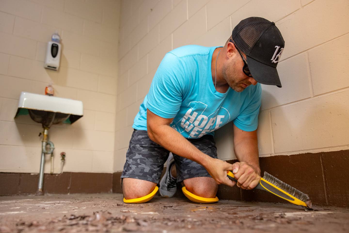 Ryan Krewer scrapes paint off of the bathroom floor in preparation for epoxy refinishing as part of Hope Week, at Kennedy Park on June 2, 2025 in Ladd.