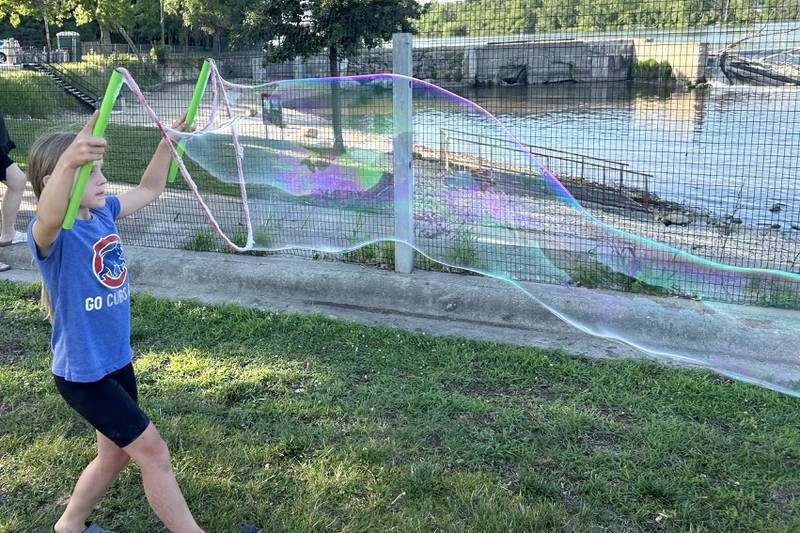 Nora Rogers, 8, of Oregon, shows how to make a very, very long bubble at the River's Edge Farmers Market in Oregon on Thursday, June 19, 2025. The bubble fun was provided by "Bubble Guy" Jason Kollom, who was sponsored by the Oregon Public Library. The Farmers Market is held Thursday nights 5-7:30 p.m. at 123 N. 2nd St., in Oregon.