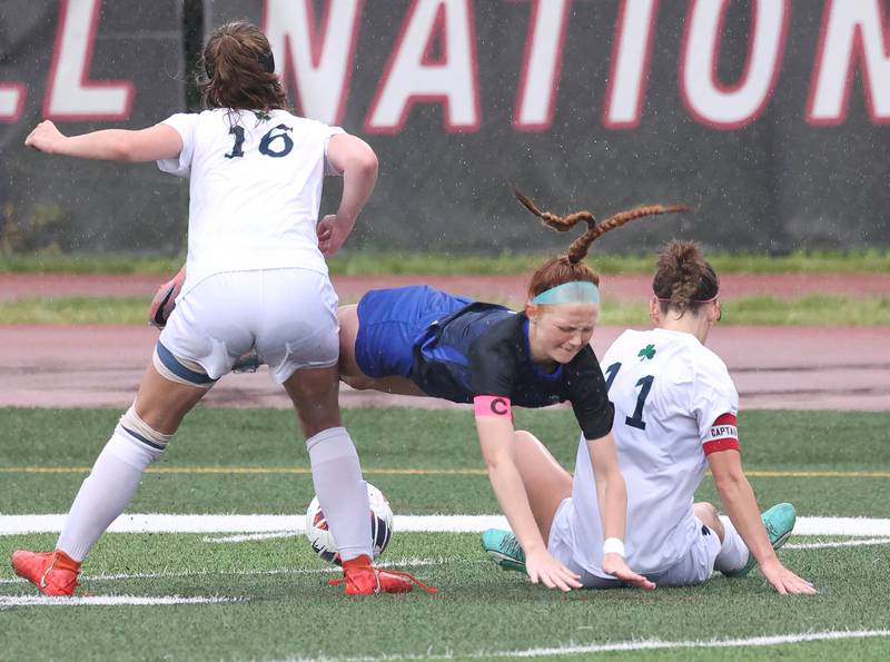 Burlington Central's Rylee Butler (middle) takes a tumble while trying to steal the ball from two Peoria Notre Dame players during their third place game Saturday, June 1, 2024, at the IHSA Class 2A state soccer finals at North Central College in Naperville.