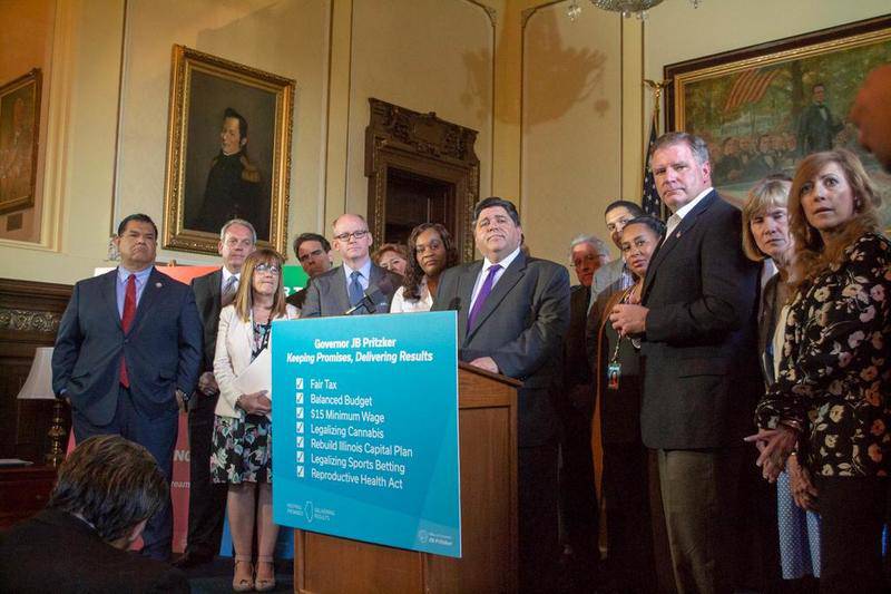 Gov. J.B. Pritzker stands among a bipartisan group of senators in his Capitol office Sunday after the Senate gave bipartisan approval to several of his key initiatives to close out the legislative session.