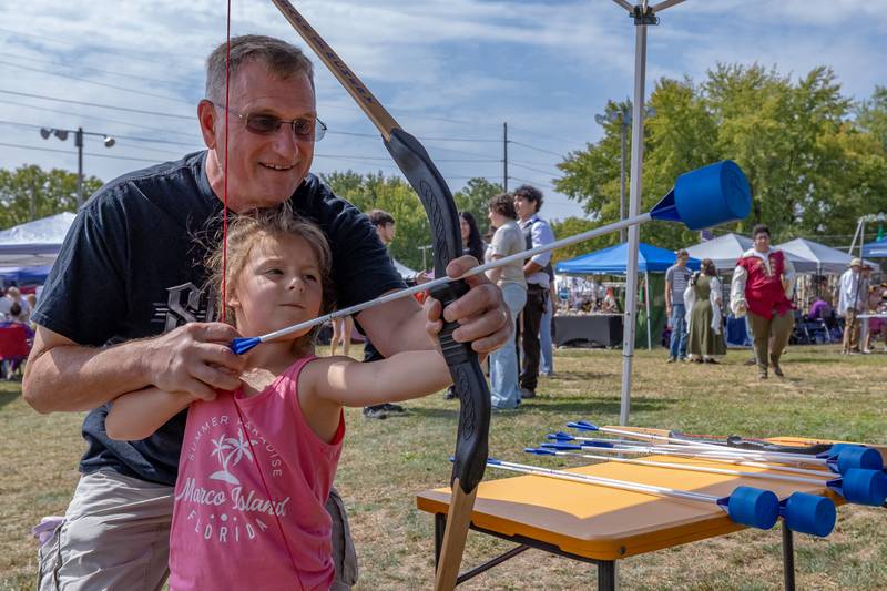 Guy Mereness helps Valyn Roumi, 5, aim a bow and arrow downrange at a target at the Marseilles Renaissance Faire on September 13, 2025 in Marseilles.