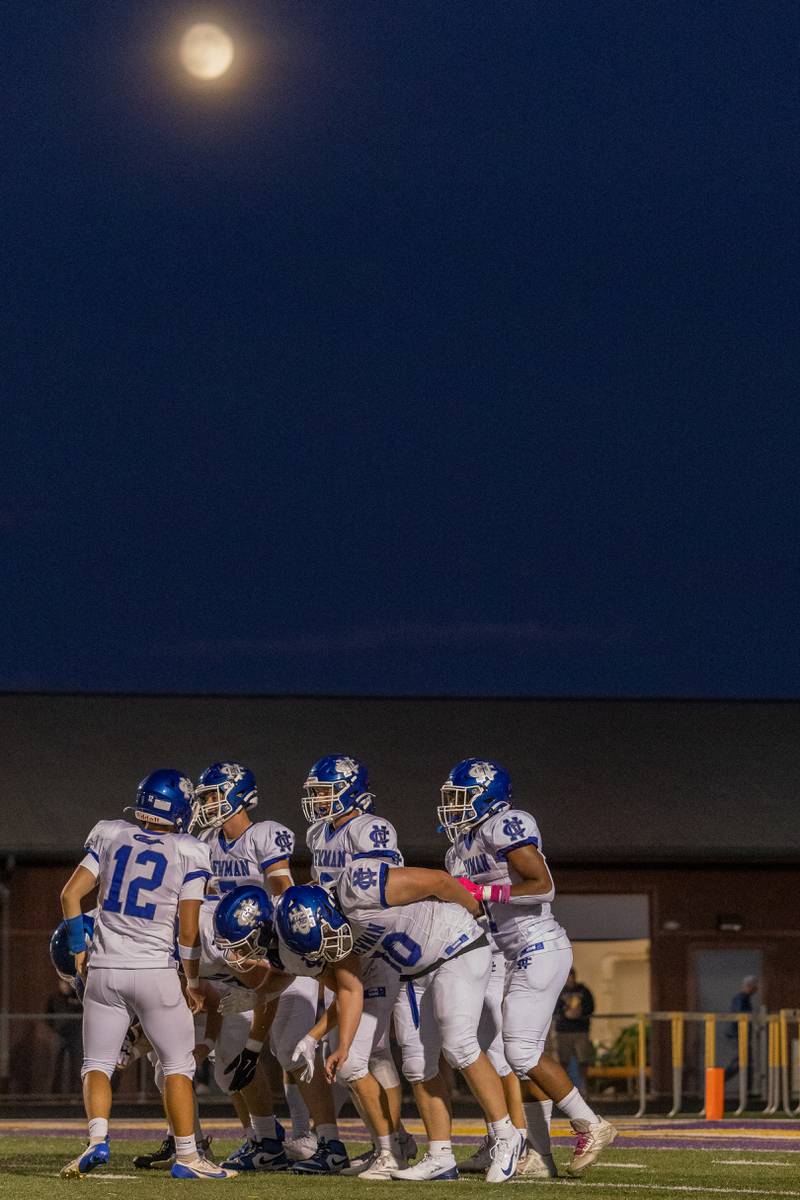 Newman Central Catholic athletes discuss the next play under a rising full moon during the game at The Jeff Prusator Athletic Complex on September 5, 2025 at Mendota High School.