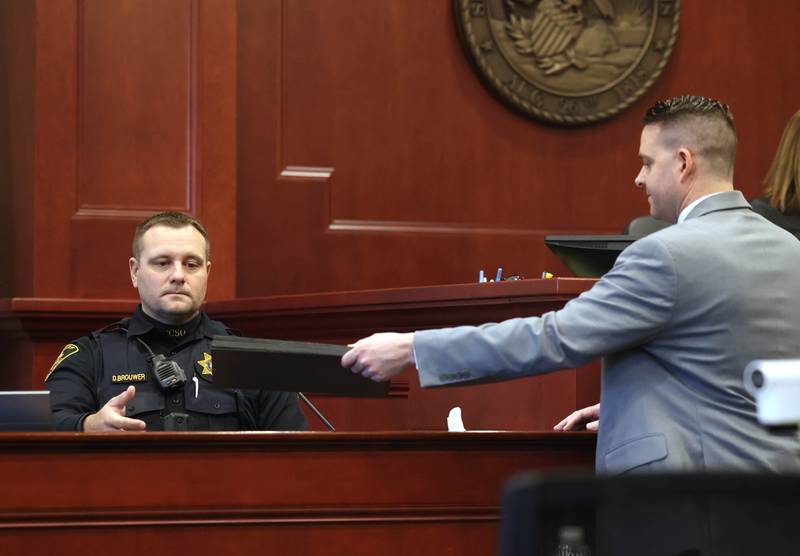 DeKalb County Sheriff’s Deputy Douglas Brouwer (left) testifies in response to evidence presented to him by prosecutor Neil Michling (right) during the trial of Jonathan Hurst Thursday, Jan. 23, 2025, at the DeKalb County Courthouse. Brouwer testified about what he saw upon arrival at the scene where Sycamore elderly mother and son Patricia and Robert Wilson were found dead. Hurst is charged in the 2016 slayings of the Wilsons.