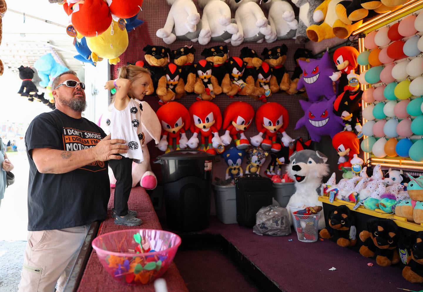Two-year-old Elizabeth Sunday, of Cabery, winds up to throw a dart to win a prize with help from her papa, Tim Lowe, of Kankakee, at the Kankakee County Fair on Saturday, Aug. 2, 2025.