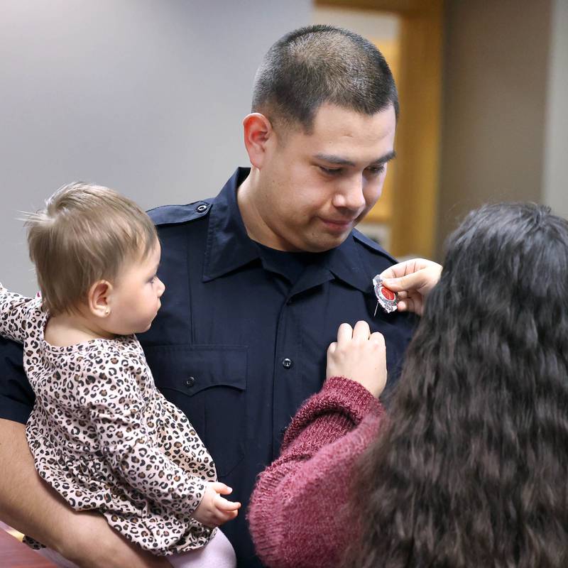 New Sycamore firefighter Carlos Aburto has his badge pinned on by girlfriend Stephanie Starks as he holds daughter Sophia Aburto following being officially sworn in Monday, April 1, 2024, during the Sycamore City Council meeting in the chambers at Sycamore Center.