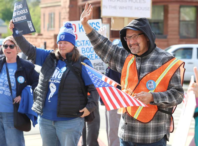 Protesters wave at passing vehicles Friday, May 1, 2026, during a May Day rally at Memorial Park in downtown DeKalb. The group gathered to advocate for workers’ rights and push for billionaires to be taxed amid cost-of-living burdens they argue are hurting everyday Americans.