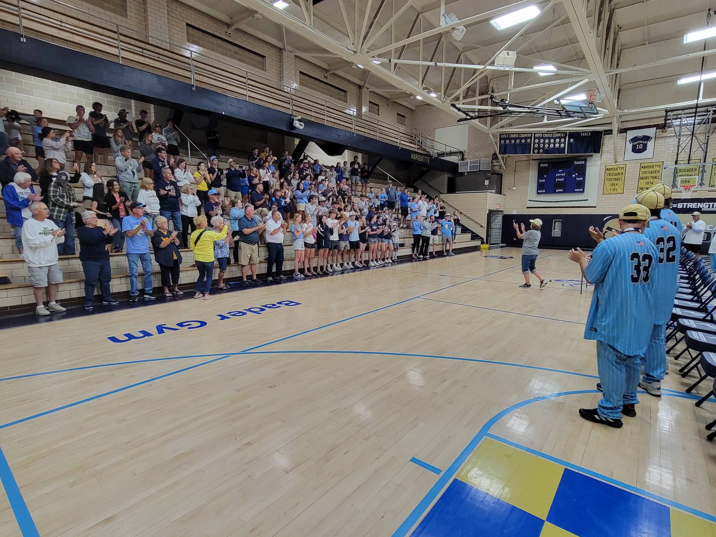 Marquette superfan Jo Parrott leads the Crusaders baseball team and the welcoming assembly in the school song Saturday at Bader Gym in Ottawa.