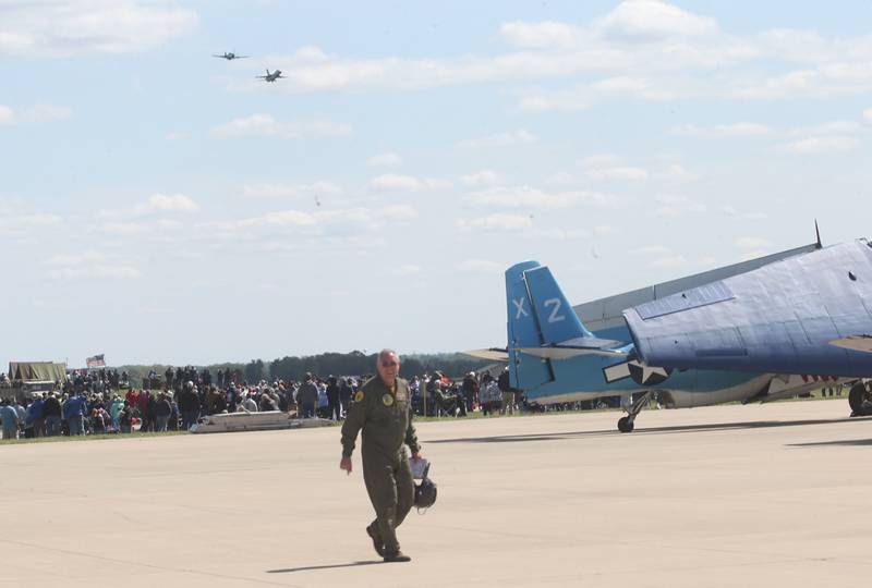 A pilot walks to his TBM aircraft as a P-51 Mustang flies with the Viper F-16 Demo Team aircraft during the 10th annual TBM Avenger Reunion and Airshow on Friday, May 16, 2025 at the Illinois Valley Regional Airport in Peru.