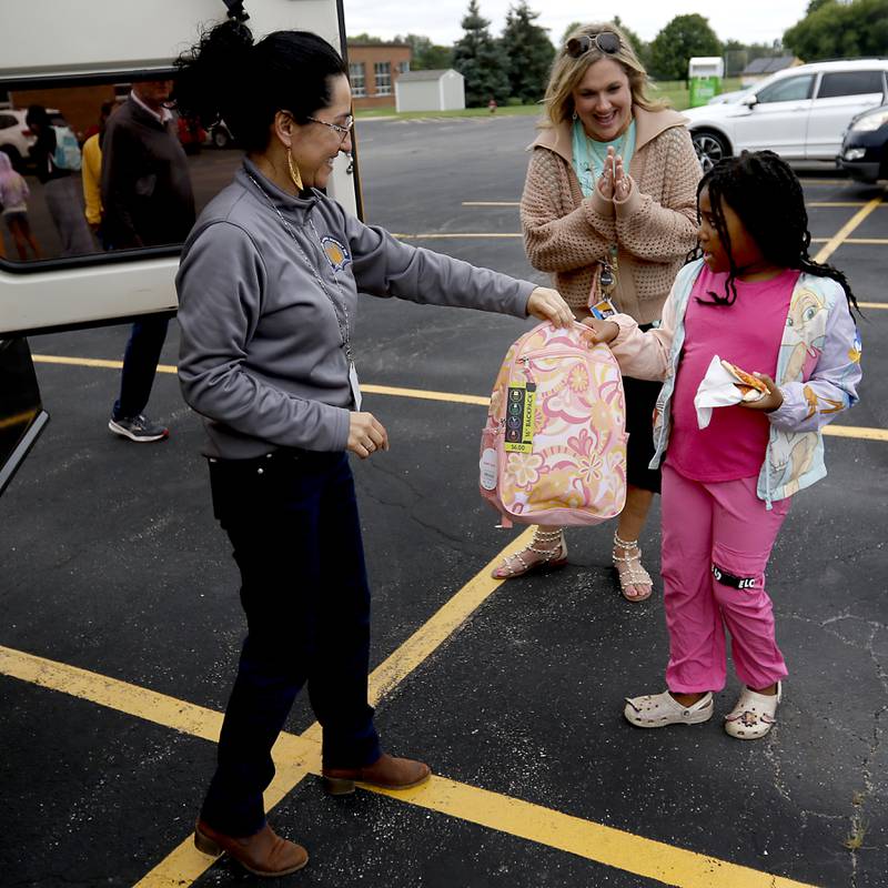 Gabi Ordonez hands JaKayla Ruffin an backpack during a Woodstock School District 200 Back to School Coming to You event at Northwood Middle School on Tuesday, Aug. 6, 2024. The location was one of twelve stops on the tour that gave out backpacks and school supplies, provided registration help and computer repair.