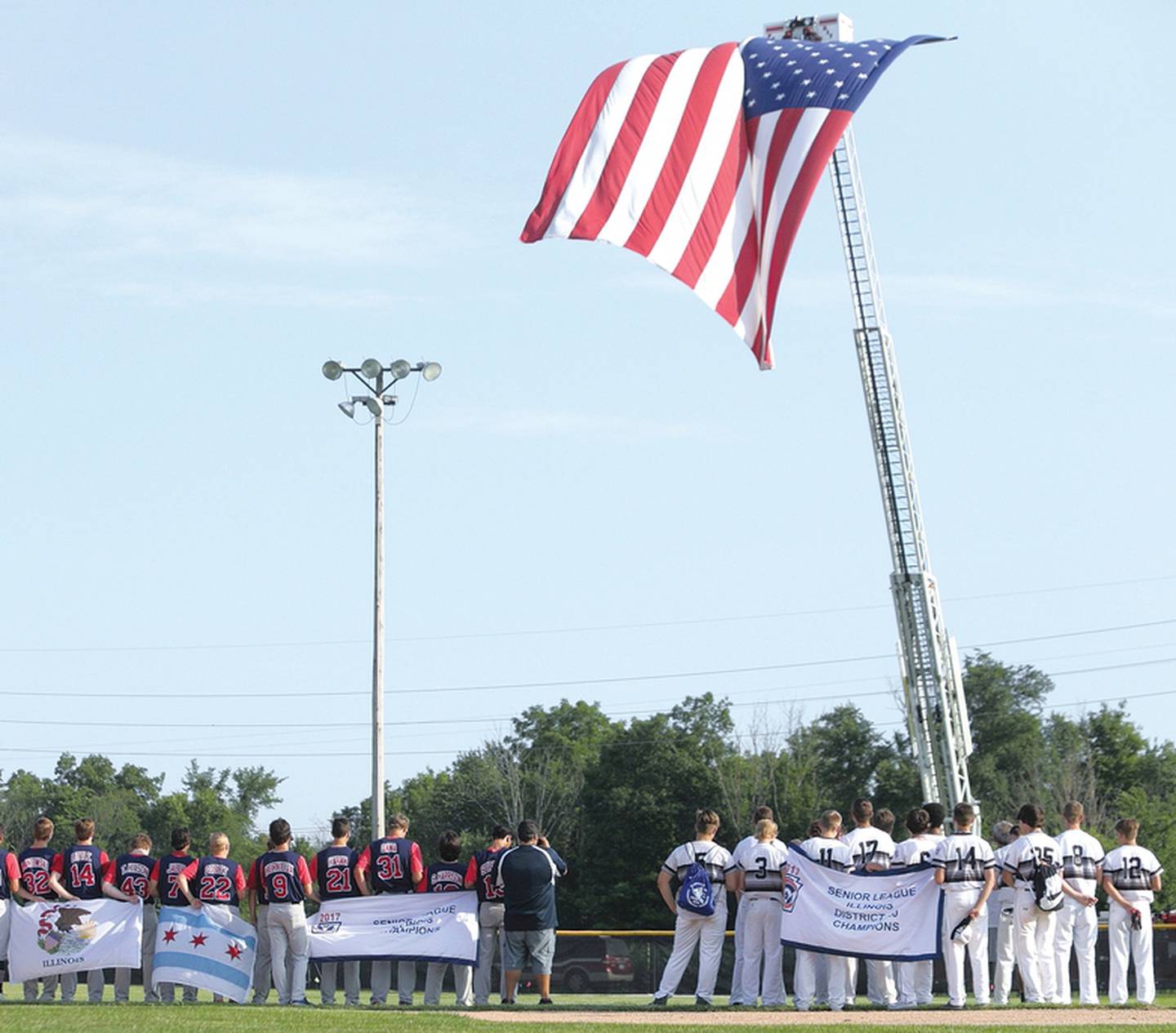 Members of District 20 Senior League champion Ottawa (right) and Illinois state champion Clear Ridge stand in front of a giant flag provided by the City of Peru during the playing of the national anthem at a past Central Region Section tournament hosted by District 20 Little League.
