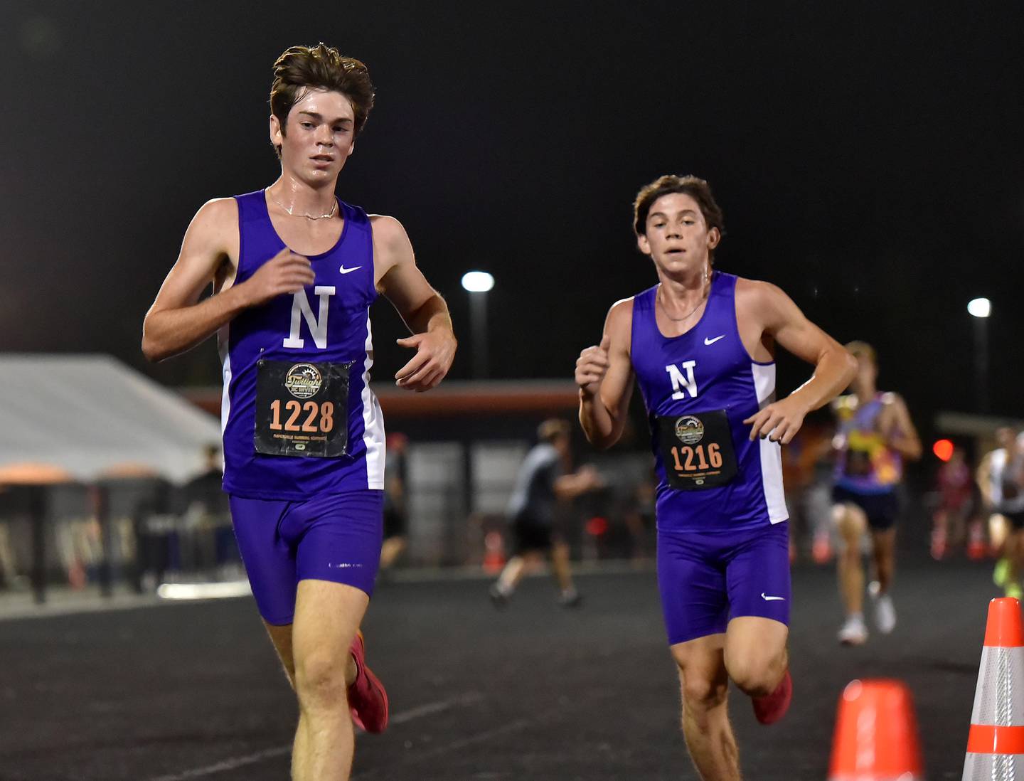 Downers Grove North’s Ryan Eddington, left, and Grant Schroder battle to the finish at the Naperville Twilight Cross Country meet at Naperville North High School on Wednesday night, October 4, 2023.