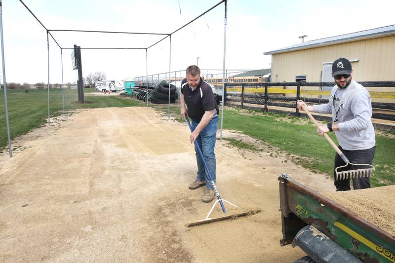 Mark Ekstrom, (left) director of buildings and grounds for Sycamore Community School District 427, and Scott Winter, warehouse manager, rake dirt into low spots Tuesday, April 11, 2023, in the batting cage behind the softball field at Sycamore High School.