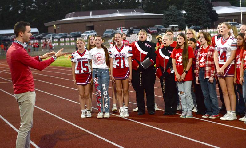 Oregon High School Choir Director Zach Hall directs choir members as they sing the National Anthem before the 2025 Homecoming football game with Rock Falls on Friday, Sept. 19, 2025 at Landers-Loomis Field in Oregon.