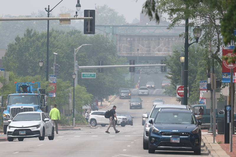 A pedestrian crosses West Jefferson Street as haze from the Canadian wildfires hangs over Joliet on Wednesday, June 28th, 2023.