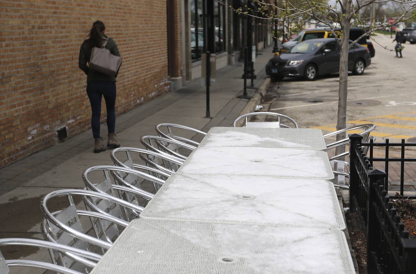 A women walks past the snow-covered tables outside Cafe Olympia in downtown Crystal Lake on Monday, April 17, 2023, after the McHenry County area received a dusting of snow overnight.