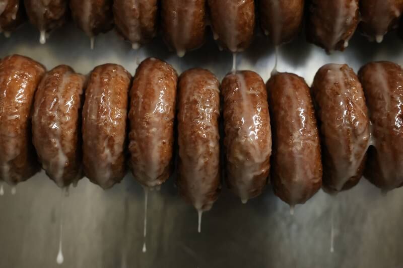 Freshly glazed cake donuts hang on a rack at Home Cut Donuts on Jefferson Street, Saturday, March 25, 2023 in Joliet.