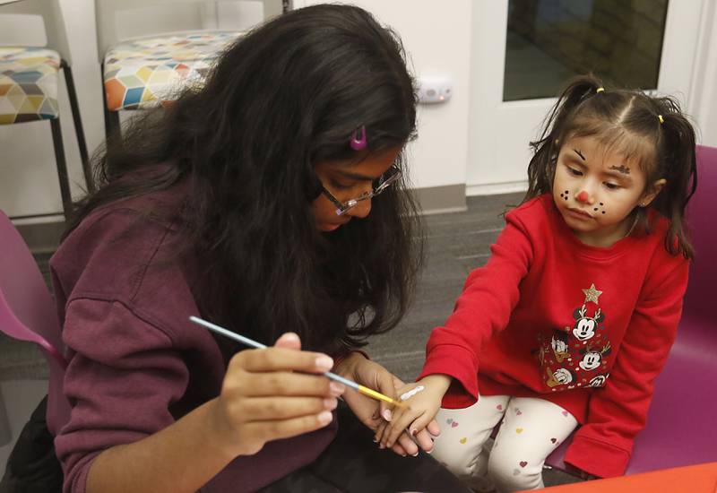 Valerie Silva, 4, of Huntley, has her hand painted by volunteer Neha Gopal on Friday, Dec. 2, 2022, during the Very Merry Huntley Holiday Open House at the Huntley Area Public Library. The event featured musical entertainment by Andy Huber, reindeer, Santa, a scavenger hunt, face painting, and a snowball toss.