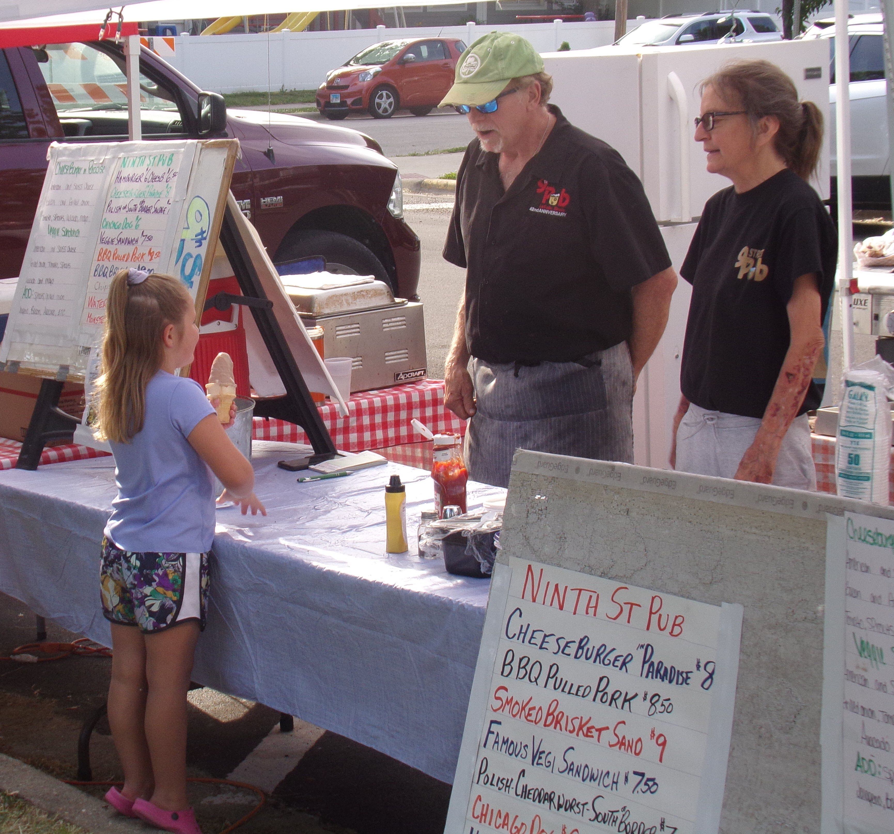 Madelyn Kadelak talks to food vendors from Ninth Street Pub as she enjoys an ice cream cone Sunday, May 28, 2023, during the Music and Art Festival at Pulaski Park in La Salle.