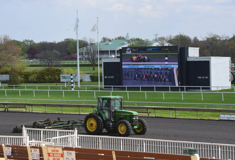 A tractor works on the track as live racing is televised on the finish line screen on the day before opening day at Arlington Park Thursday, April 29, 2021.