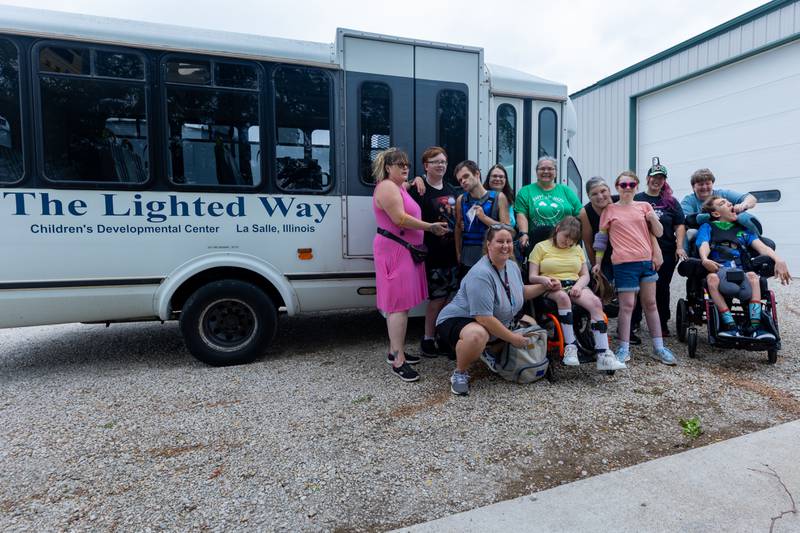 (back left to right) Jen, Joe, Tyrus, Teresa, Rene, Michelle, Laura Loch, Gina, (front left to right) Allison, Sarah, Mackenzie and Decan pose for photo in front of lighted way bus on Friday, June 27, 2025 at Loch Countryside Kennel in Peru.