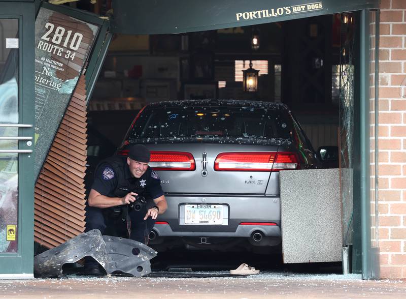 An Oswego Police officer photographs the scene Wednesday, July 30, 2025, where a car crashed through the front entrance of the Portillo’s at 2810 U.S. Route 34 in Oswego injuring 12.