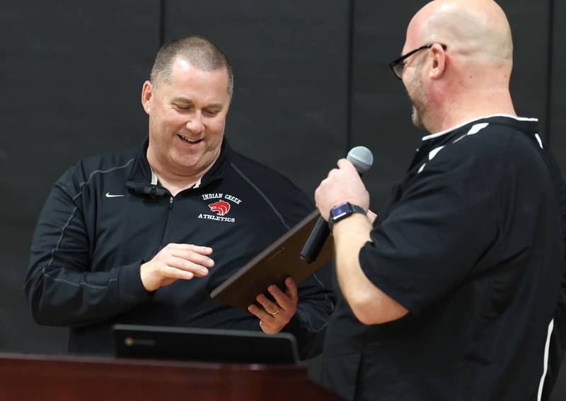 Indian Creek girls basketball head coach Paul Muchmore acceopts a plaque from athletic director Ehren Mertz Tuesday, Feb. 10, 2026, during a cermony held before Indian Creek took on Rosary. Muchmore, the longtime coach of the Timberwolves, was being honored at his last home game before retirement from coaching at the end of the season.